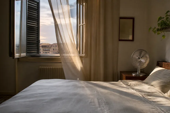 camera da letto estiva con finestra aperta, tende leggere e ventilatore