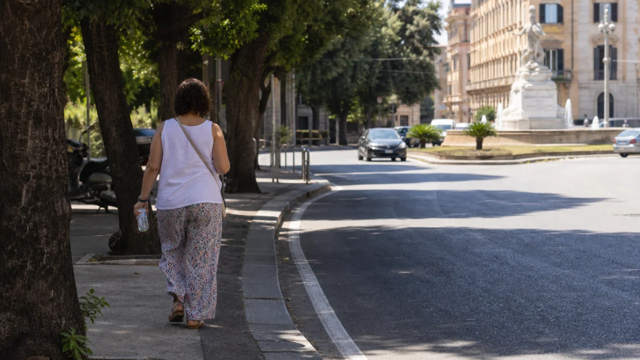Persona che cammina su un marciapiede ombreggiato in una città estiva.