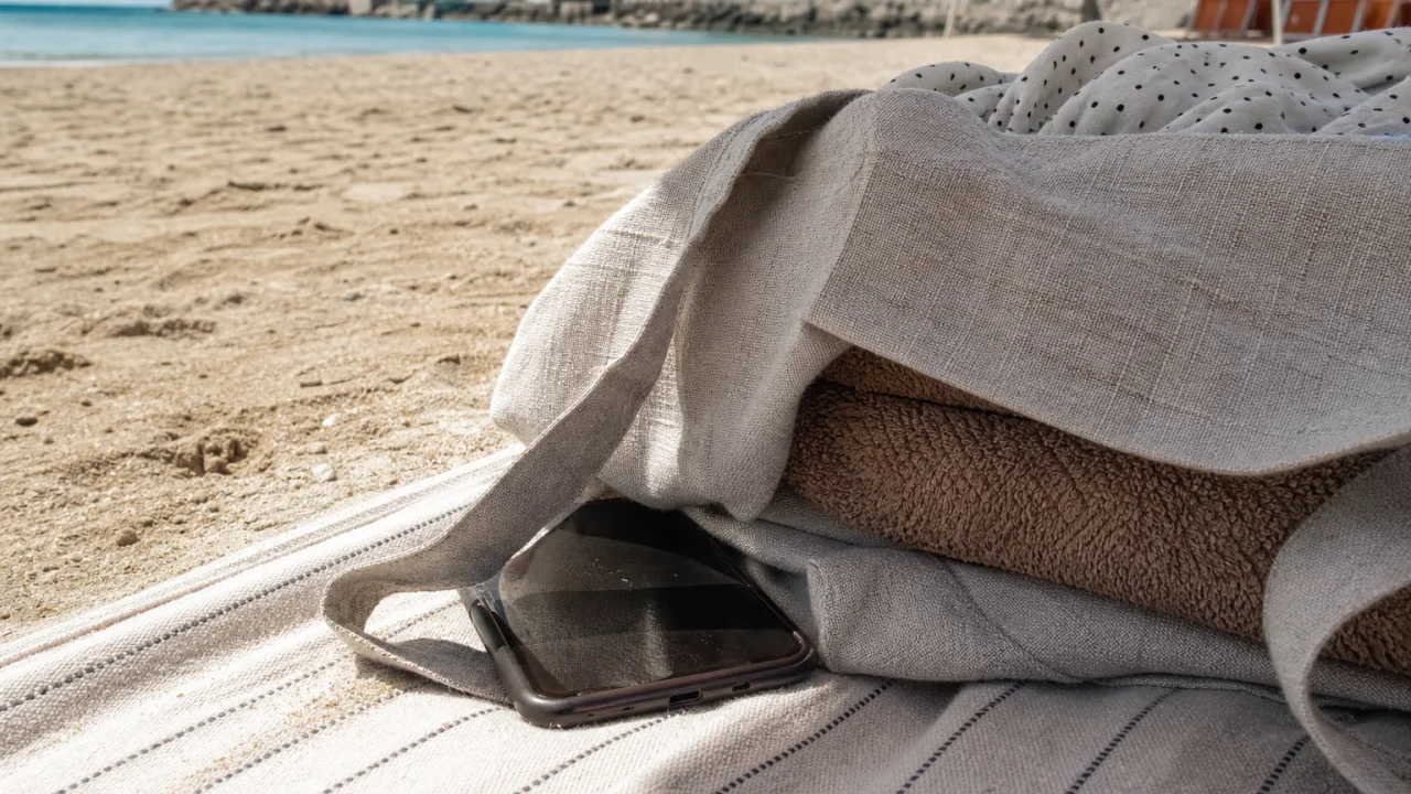 Smartphone in ombra su tavolo estivo con occhiali da sole e borraccia.