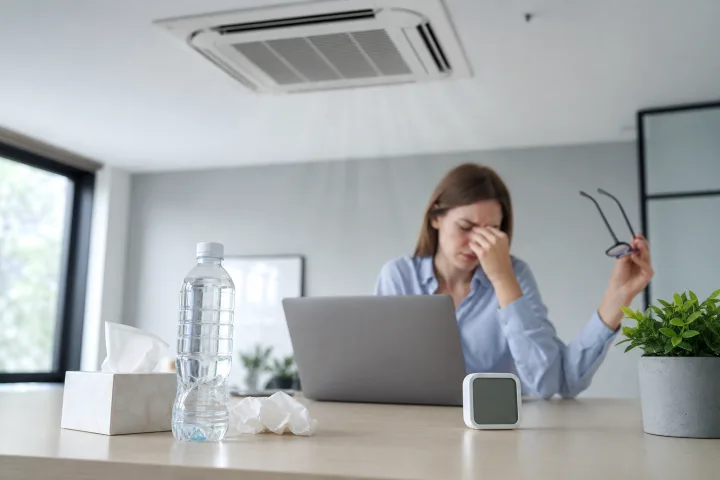 scrivania ordinata in ufficio con bocchetta dell'aria condizionata, laptop sfocato, fazzoletti e bottiglia d'acqua senza etichetta