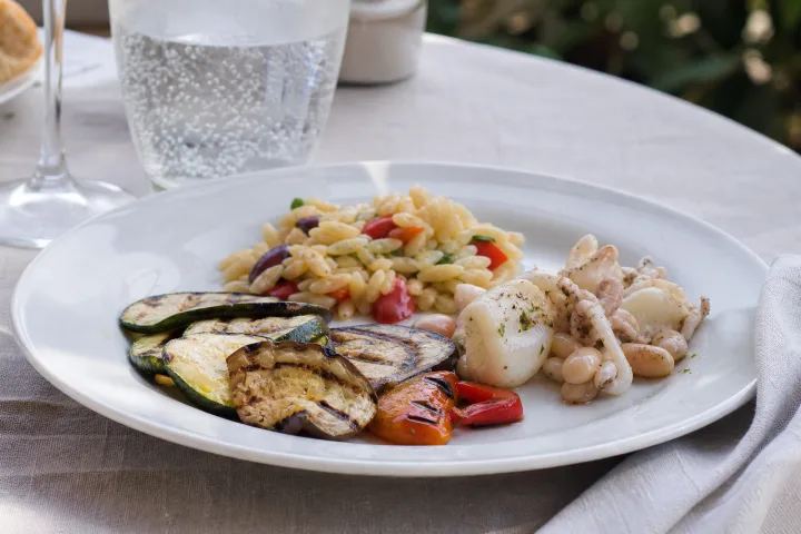 piatto estivo al ristorante con verdure grigliate, pasta e pesce su tavolo all'aperto