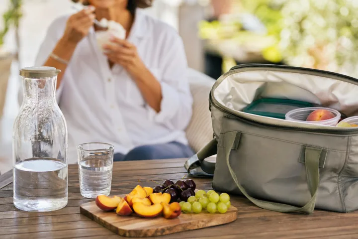 Tavolo estivo con frutta, acqua, borsa termica e coppetta piccola di gelato sullo sfondo