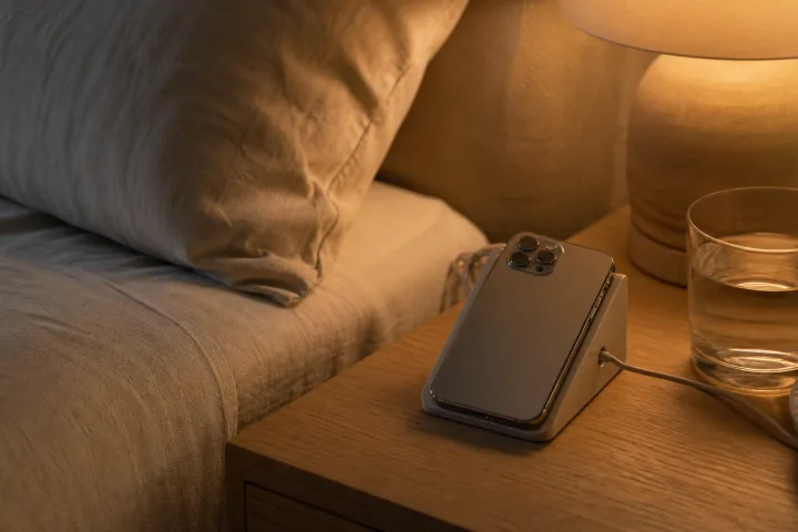 Smartphone appoggiato vicino al letto in una camera estiva con luce calda.