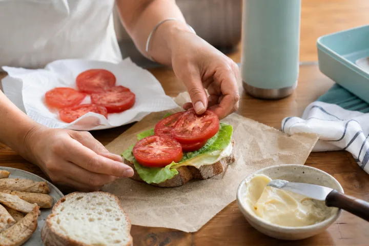 Preparazione di un panino estivo su carta alimentare con verdure asciugate e borsa termica sullo sfondo.