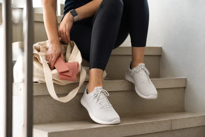 Scarpe comode senza marchi su una scala luminosa con smartwatch a schermo spento e borsa neutra