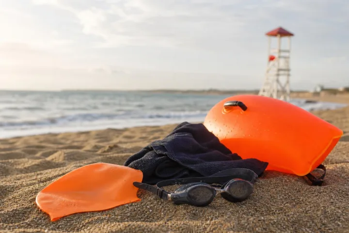 Boa arancione, cuffia e occhialini appoggiati sulla sabbia vicino al mare.