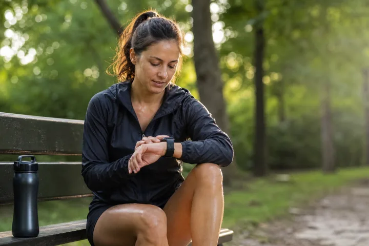 persona seduta su una panchina in un parco mentre controlla uno smartwatch dopo una corsa leggera.