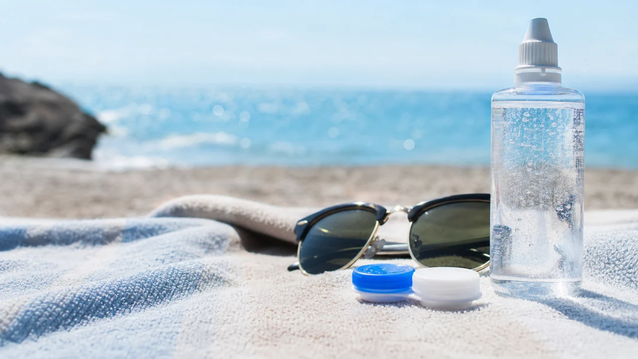 Custodia per lenti a contatto e occhiali da sole su un telo vicino al mare.