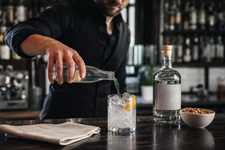 Bartender versa una bevanda analcolica con ghiaccio e limone al bancone di un bar