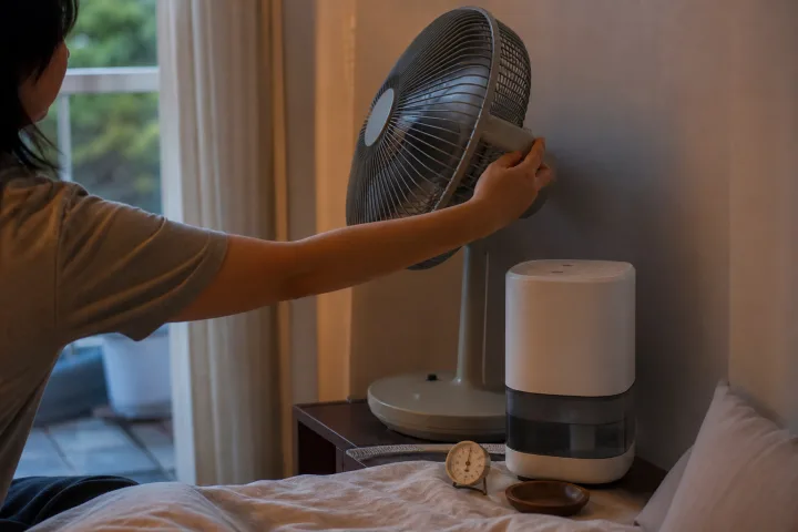 Camera estiva con ventilatore orientato verso la parete e piccolo igrometro sul comodino.