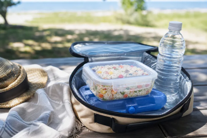 Lunch box con insalata di riso in una borsa termica aperta su un tavolo estivo all'aperto.