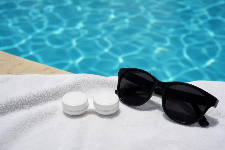 Custodia per lenti e occhiali da sole su un asciugamano accanto alla piscina.