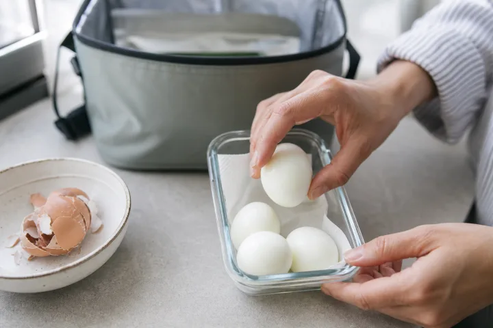 Mani che sistemano uova sode sbucciate in un contenitore ermetico su un piano cucina luminoso.
