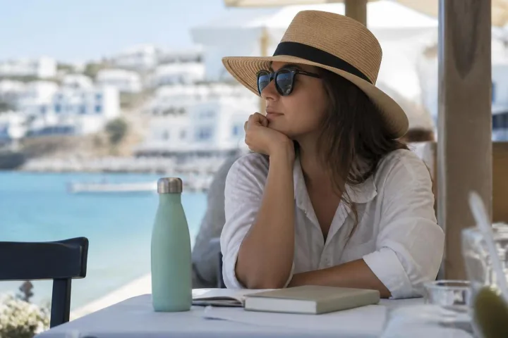Viaggiatore seduto all'ombra con acqua e cappello durante una giornata estiva al mare.